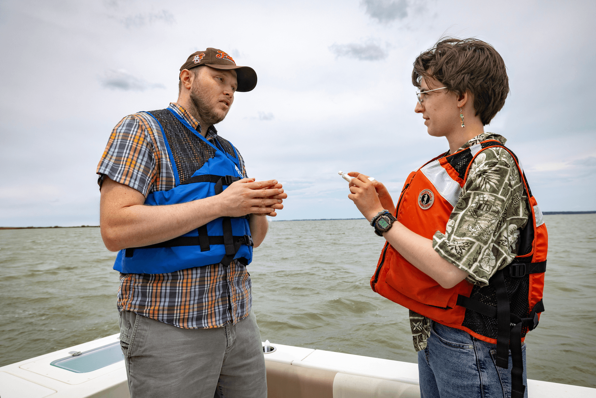 Three people bring an anchor out of the water and into a boat.