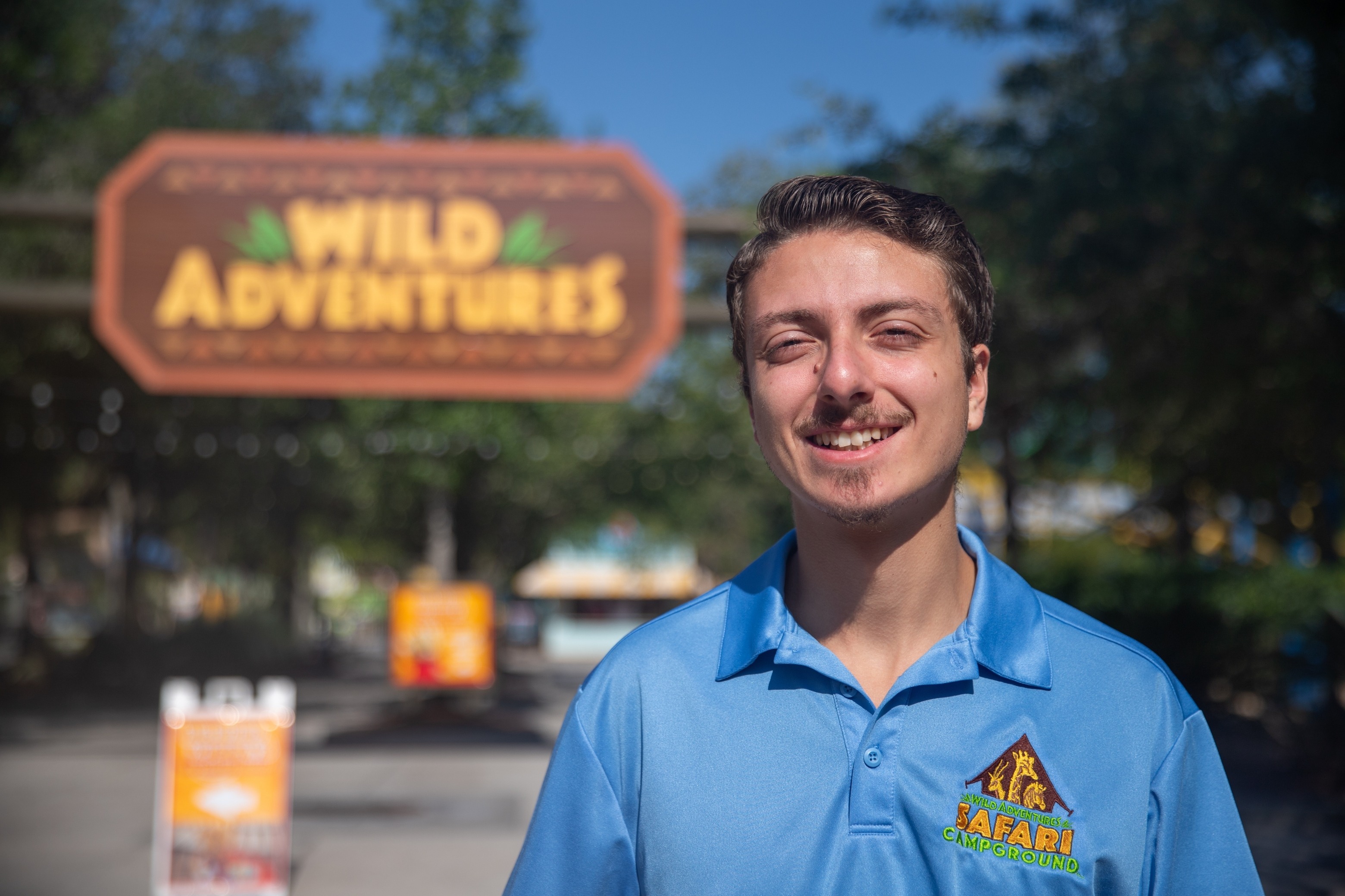A person poses for a picture next to a sign that says "Wild Adventures."