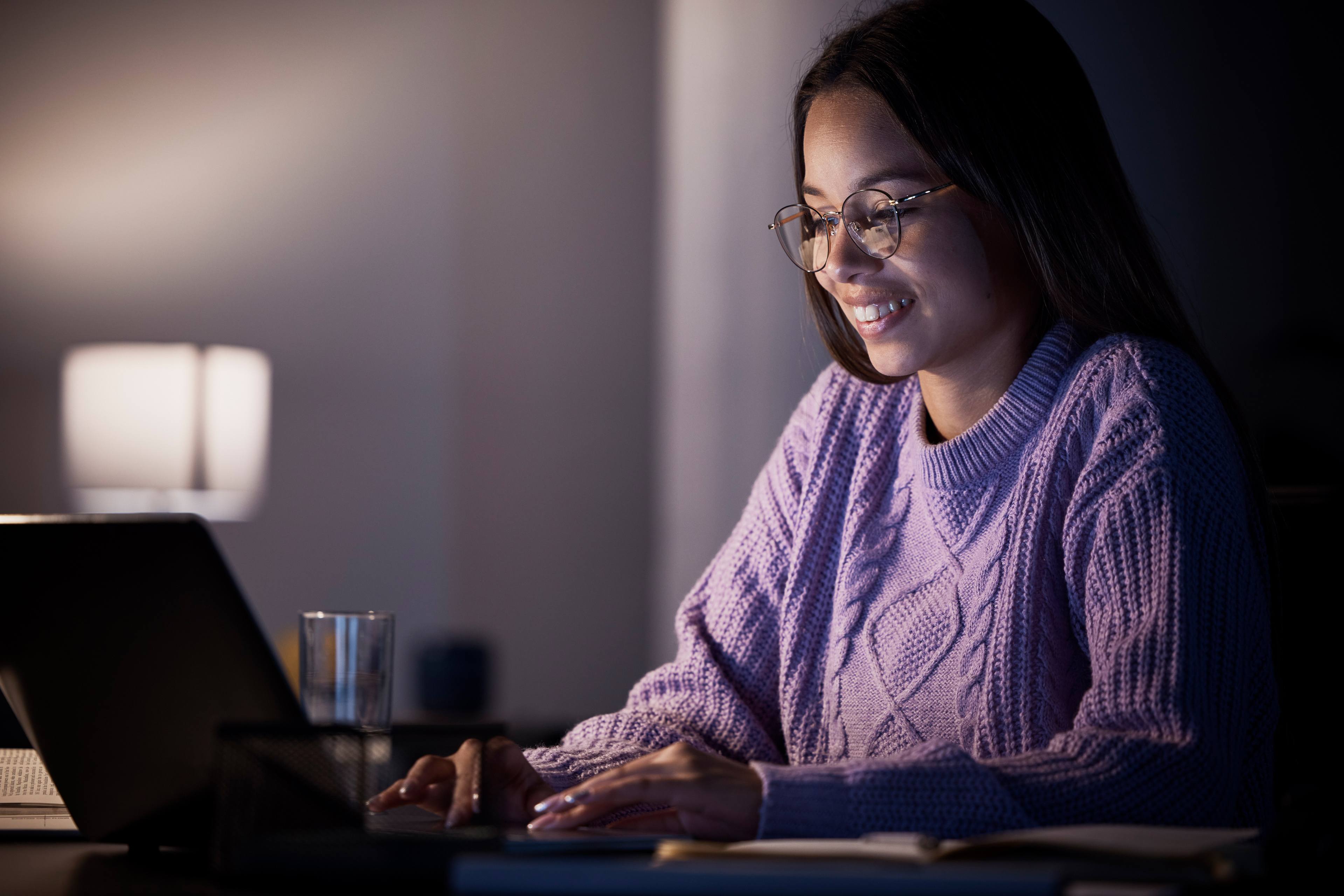 Woman, happy or laptop typing in night studying, education or homework research in living room on elearning website. Smile, student or technology in dark house for knowledge or university assignment