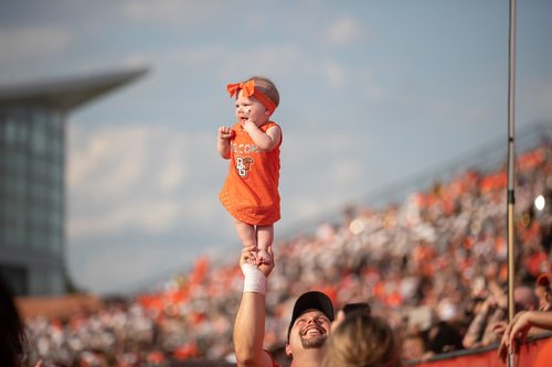 An individual holding a baby up at football game