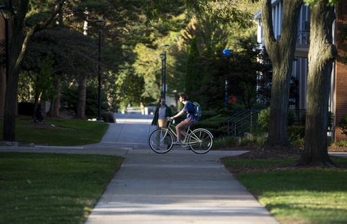 Student on bike passes in front of pedestrian on campus