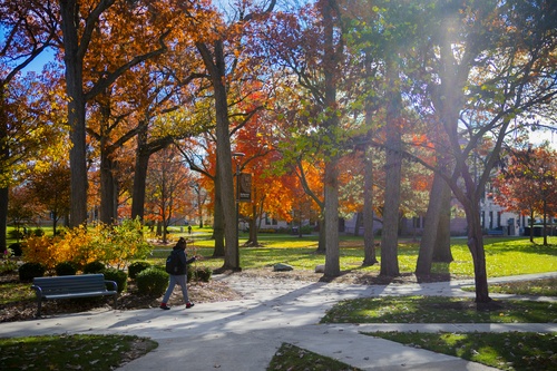 Student walking near Shatzel Hall surrounded by vibrant fall colors