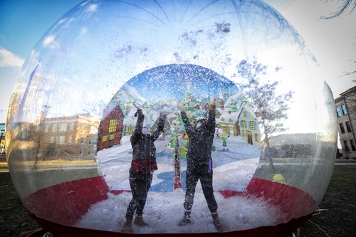 Two students raise arms in large snow globe at Winter Fest
