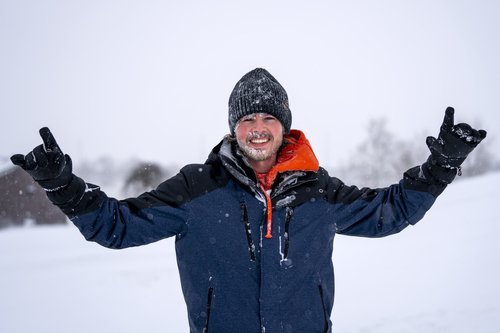 Student raises hands and smiles while snow is falling