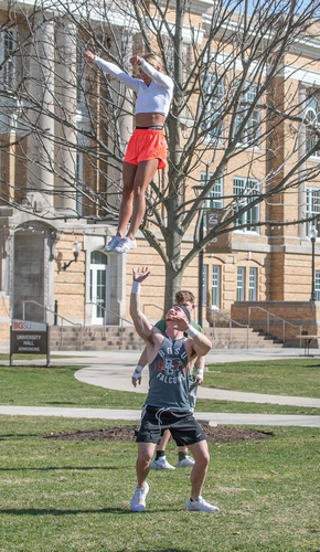 Cheerleaders perform acrobatic maneuvers in front of University Hall