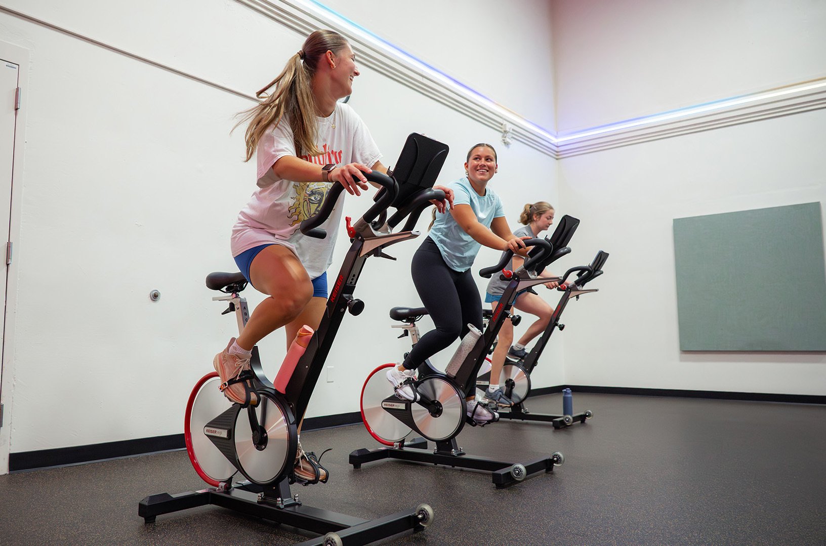 three girls riding stationary bikes during a cycling group exercise class in a studio