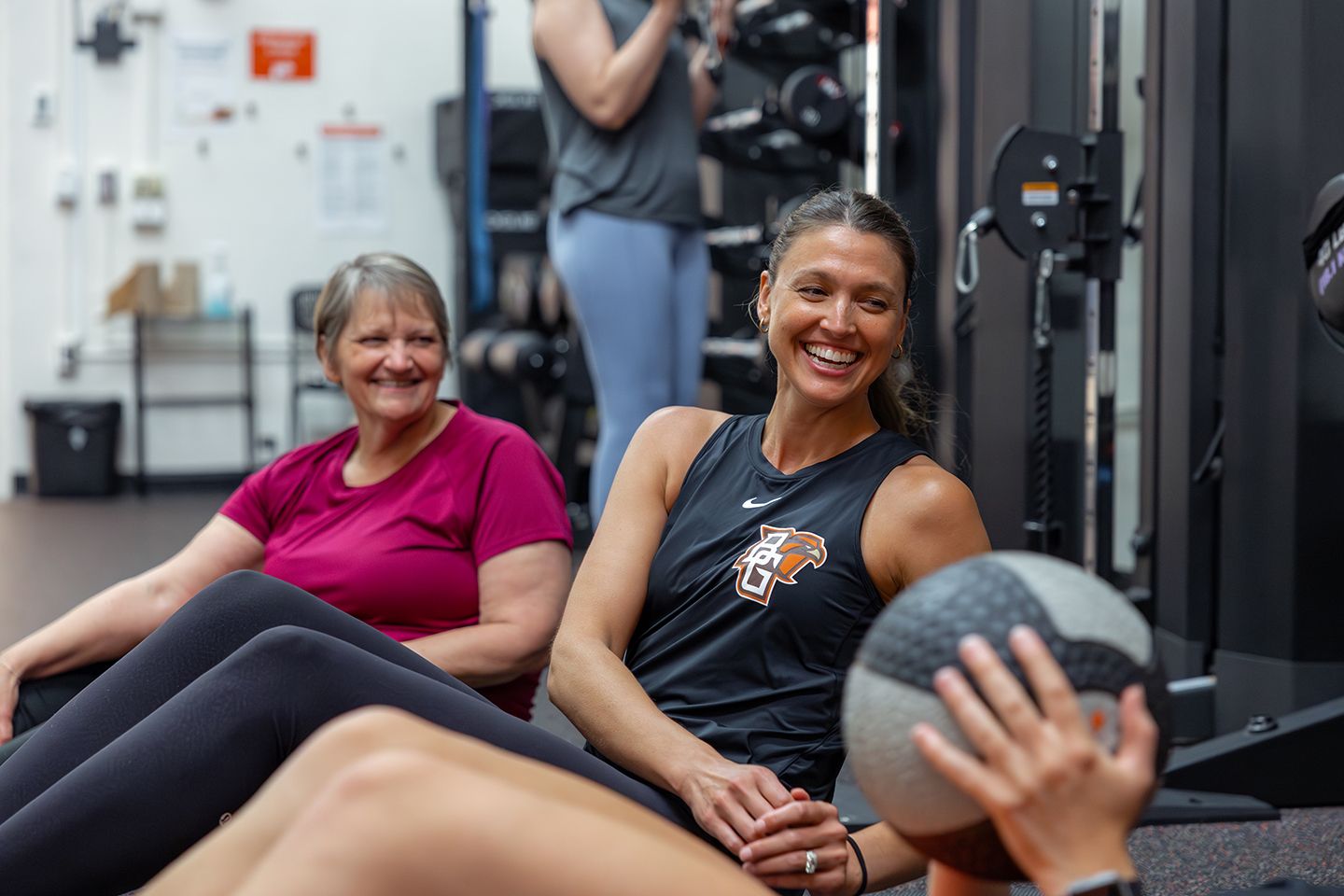 Two women in a small group training class sitting on the ground waiting to receive a weighted slam ball