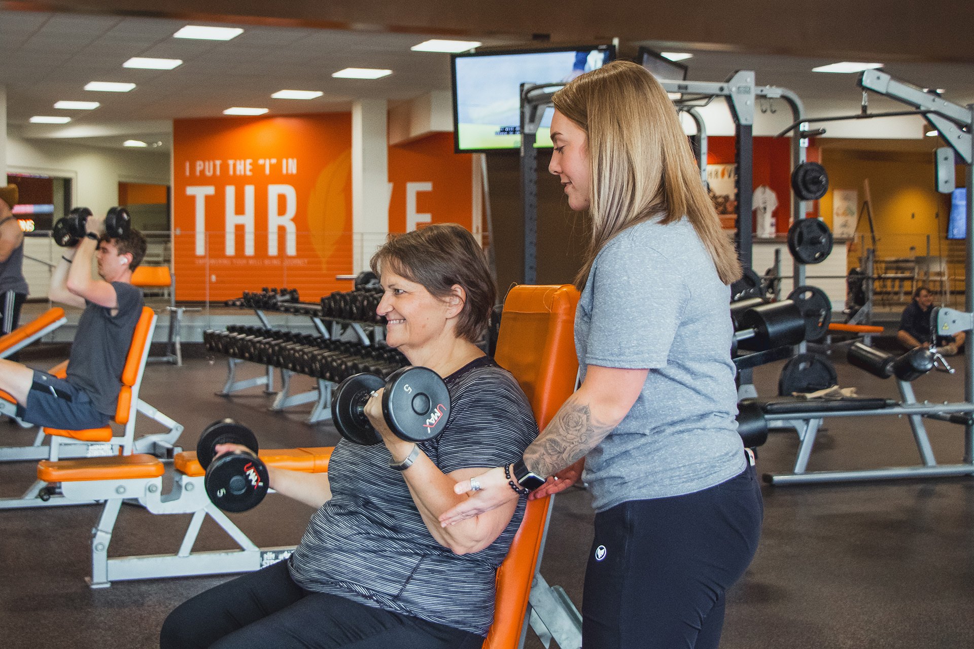a woman doing seated dumbbell curls in a gym with a personal trainer