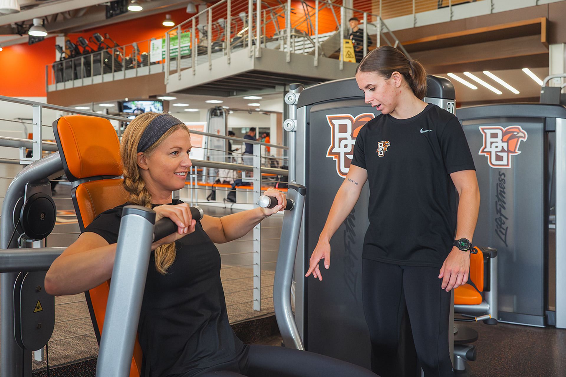 a personal trainer working with a woman at a gym on how to use a chest press machine
