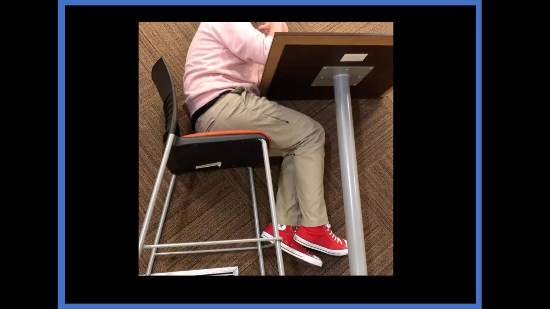 Photo of side of person from shoulder down sitting at a school desk]