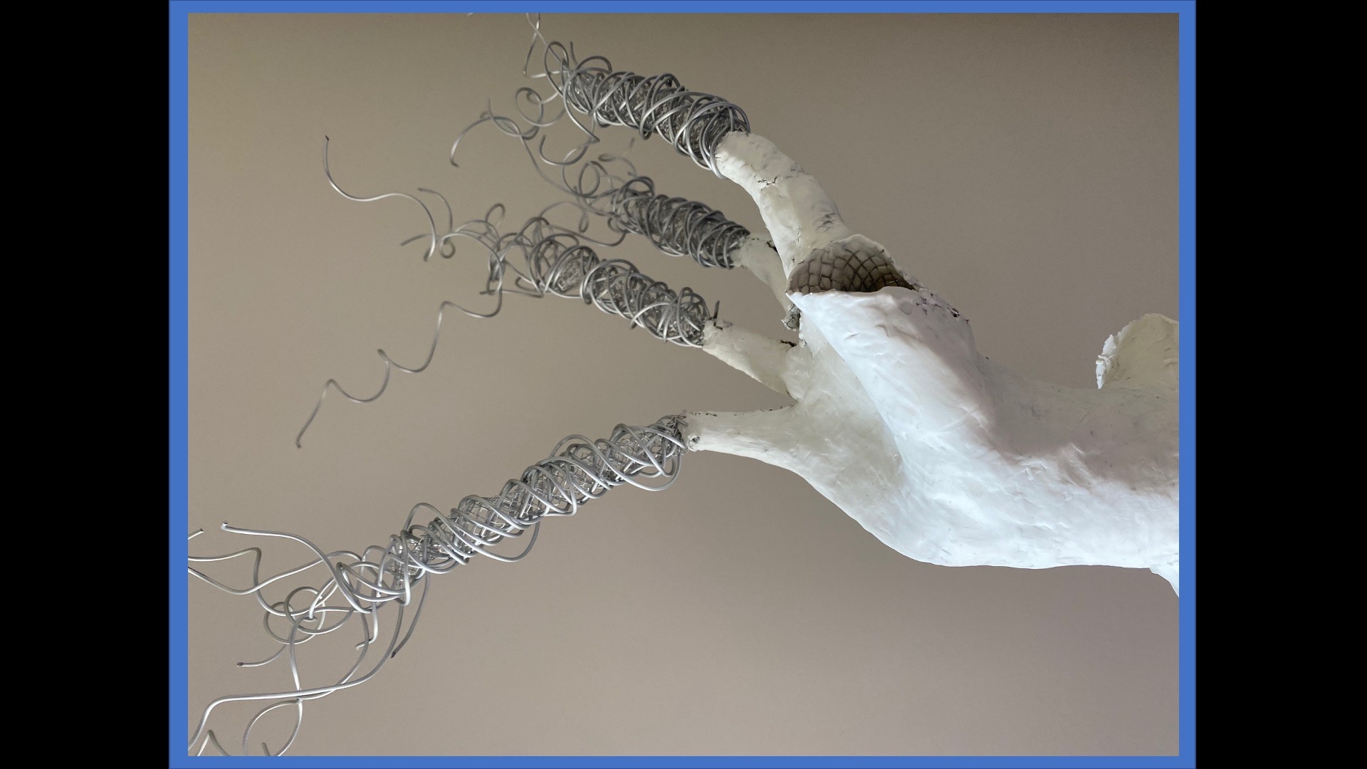 close-up photo plaster cast sculpture of damaged hollow hand with long twisting wire coil extensions from fingersof a mouth with thick white goop put on lips by a finger